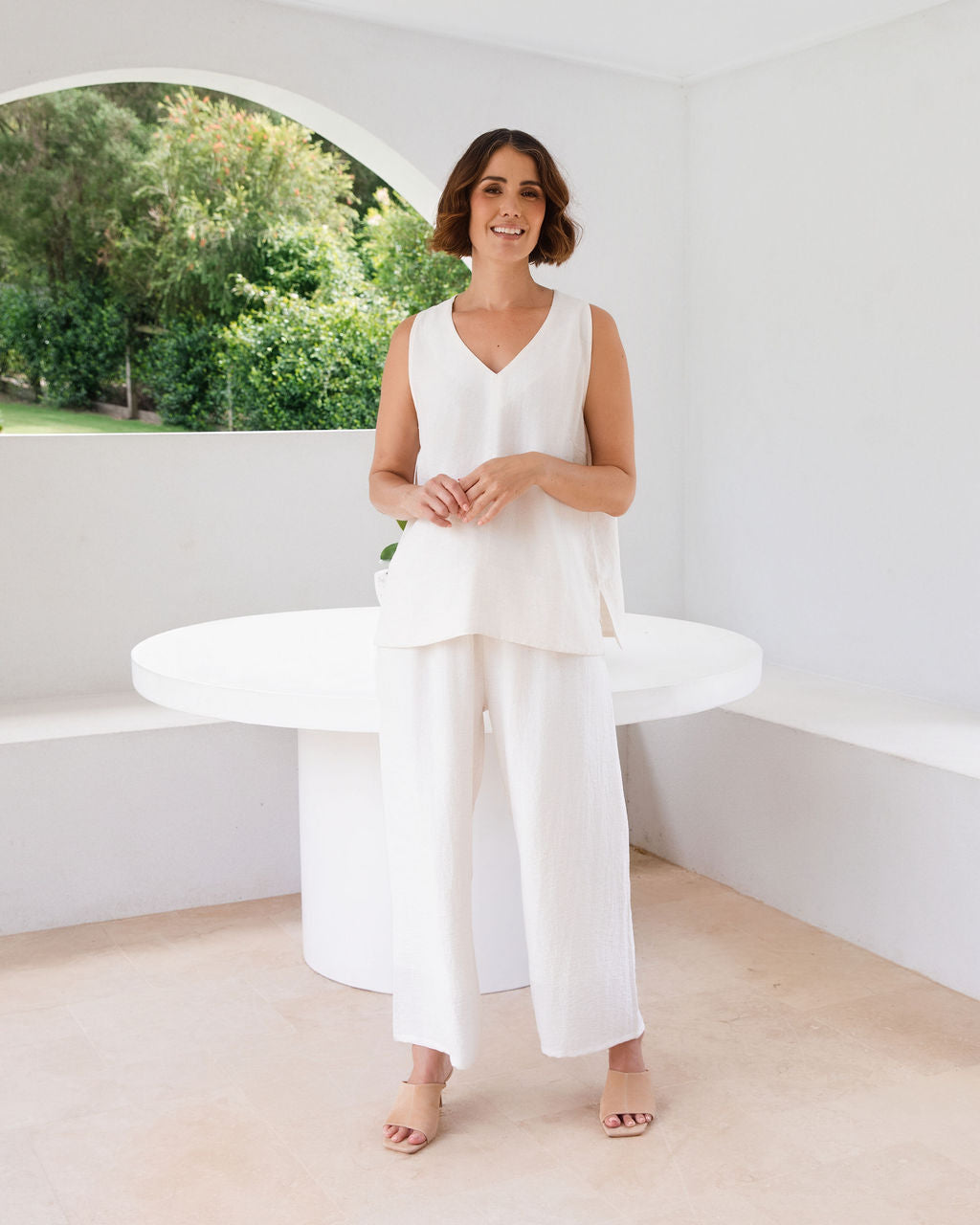 Model wearing See Saw Matching tank and pant in natural in linen and rayon blend. standing in an outdoor architecturally designed patio.