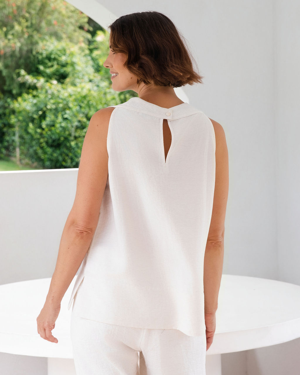 Model wearing See Saw Matching tank and pant in natural in linen and rayon blend. standing in an outdoor architecturally designed patio.