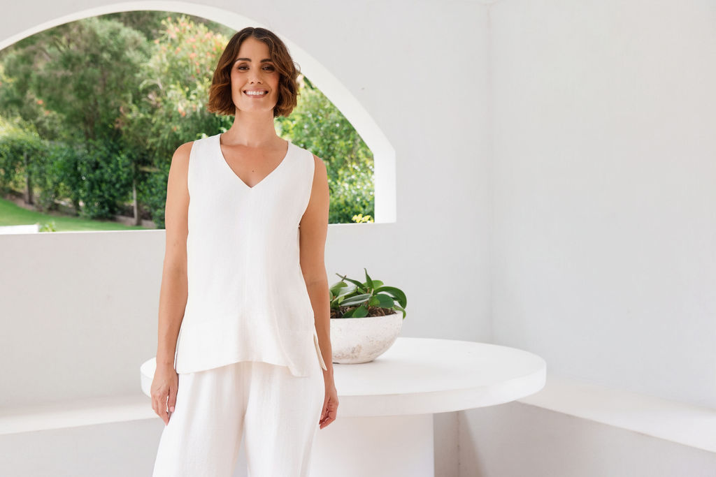 Model wearing See Saw Matching tank and pant in natural in linen and rayon blend. standing in an outdoor architecturally designed patio.