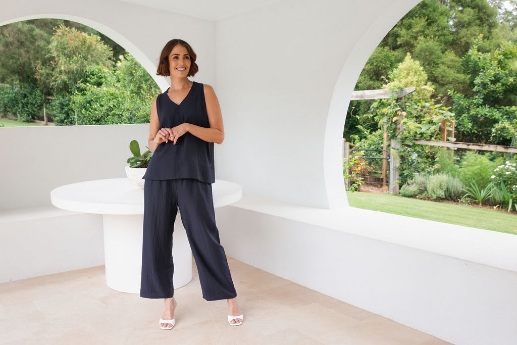 Model wearing See Saw Matching tank and pant in navy in linen and rayon blend. standing in an outdoor architecturally designed patio.