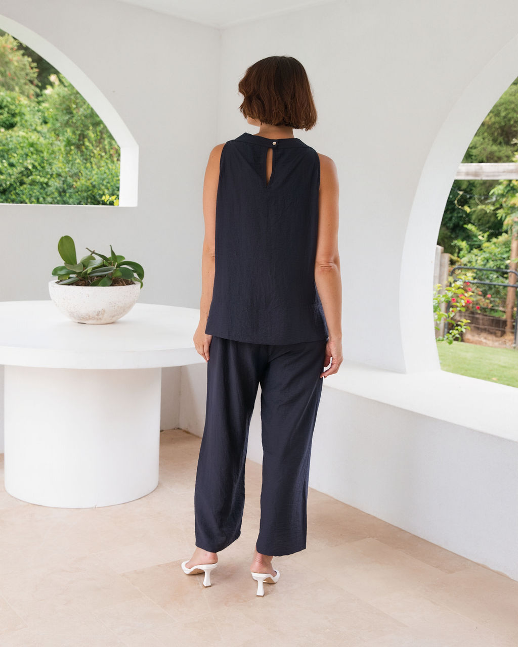 Model wearing See Saw Matching tank and pant in navy in linen and rayon blend. standing in an outdoor architecturally designed patio.