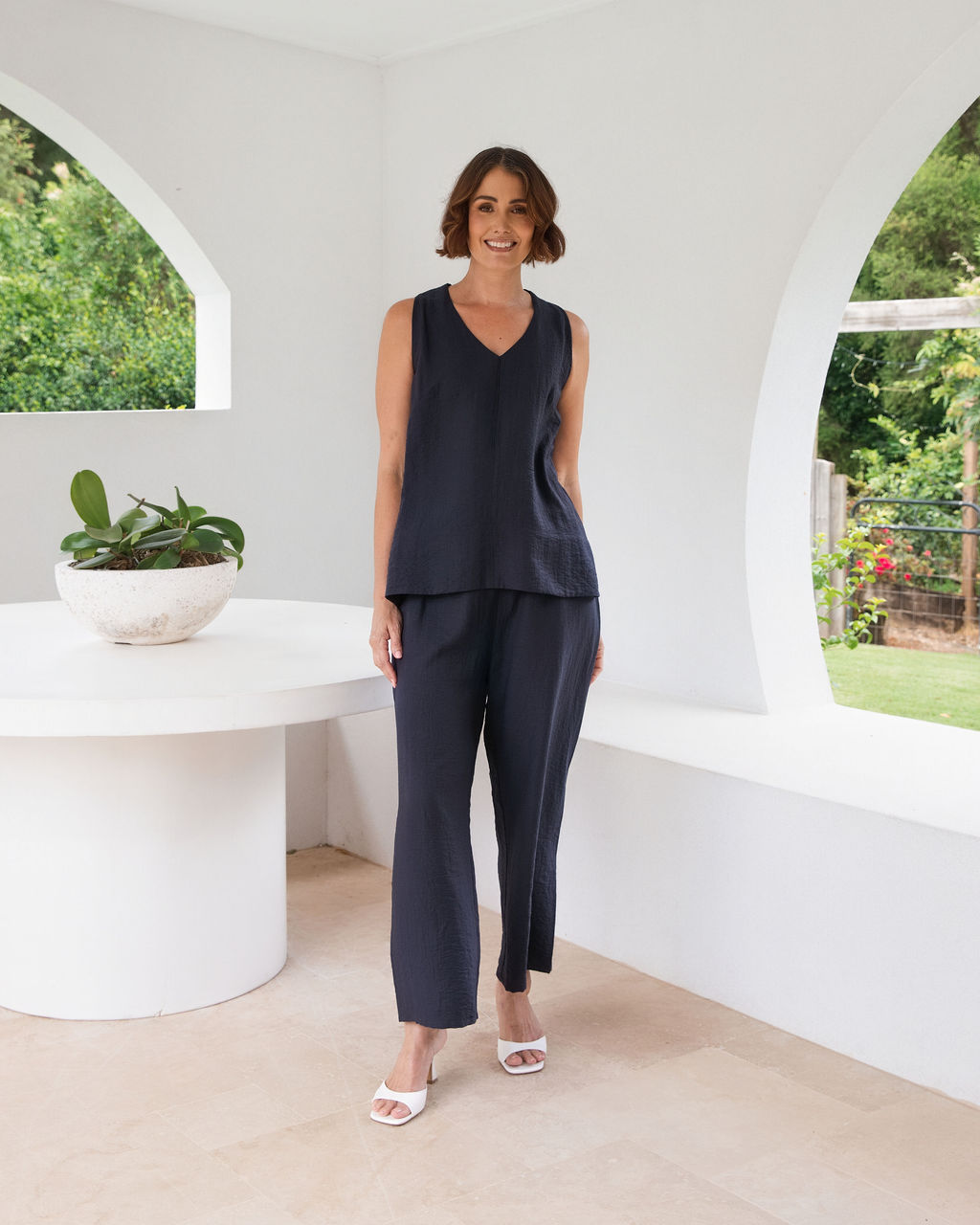Model wearing See Saw Matching tank and pant in navy in linen and rayon blend. standing in an outdoor architecturally designed patio.