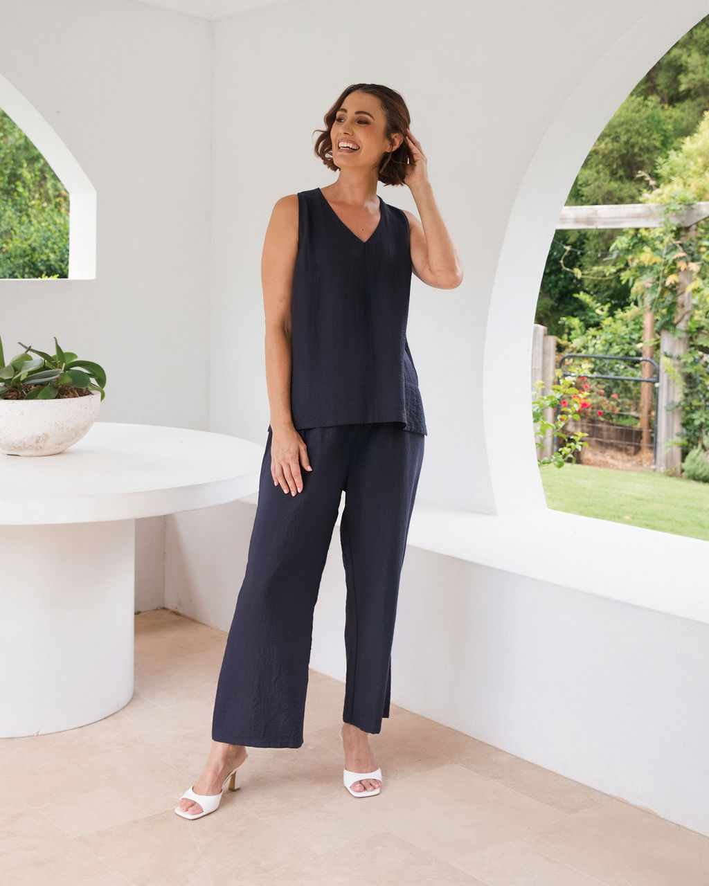 Model wearing See Saw Matching tank and pant in navy in linen and rayon blend. standing in an outdoor architecturally designed patio.