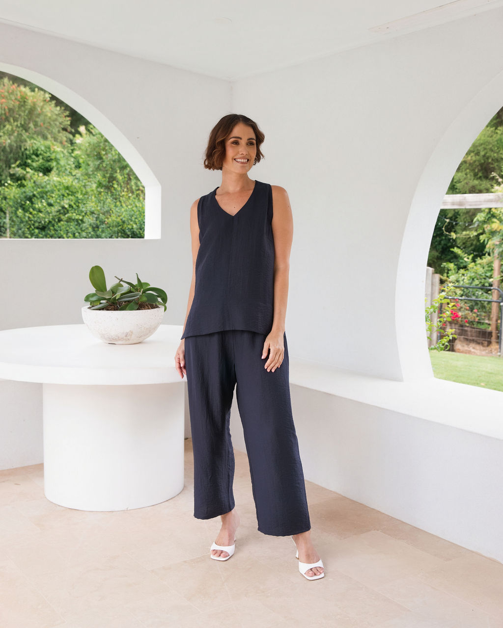 Model wearing See Saw Matching tank and pant in navy in linen and rayon blend. standing in an outdoor architecturally designed patio.