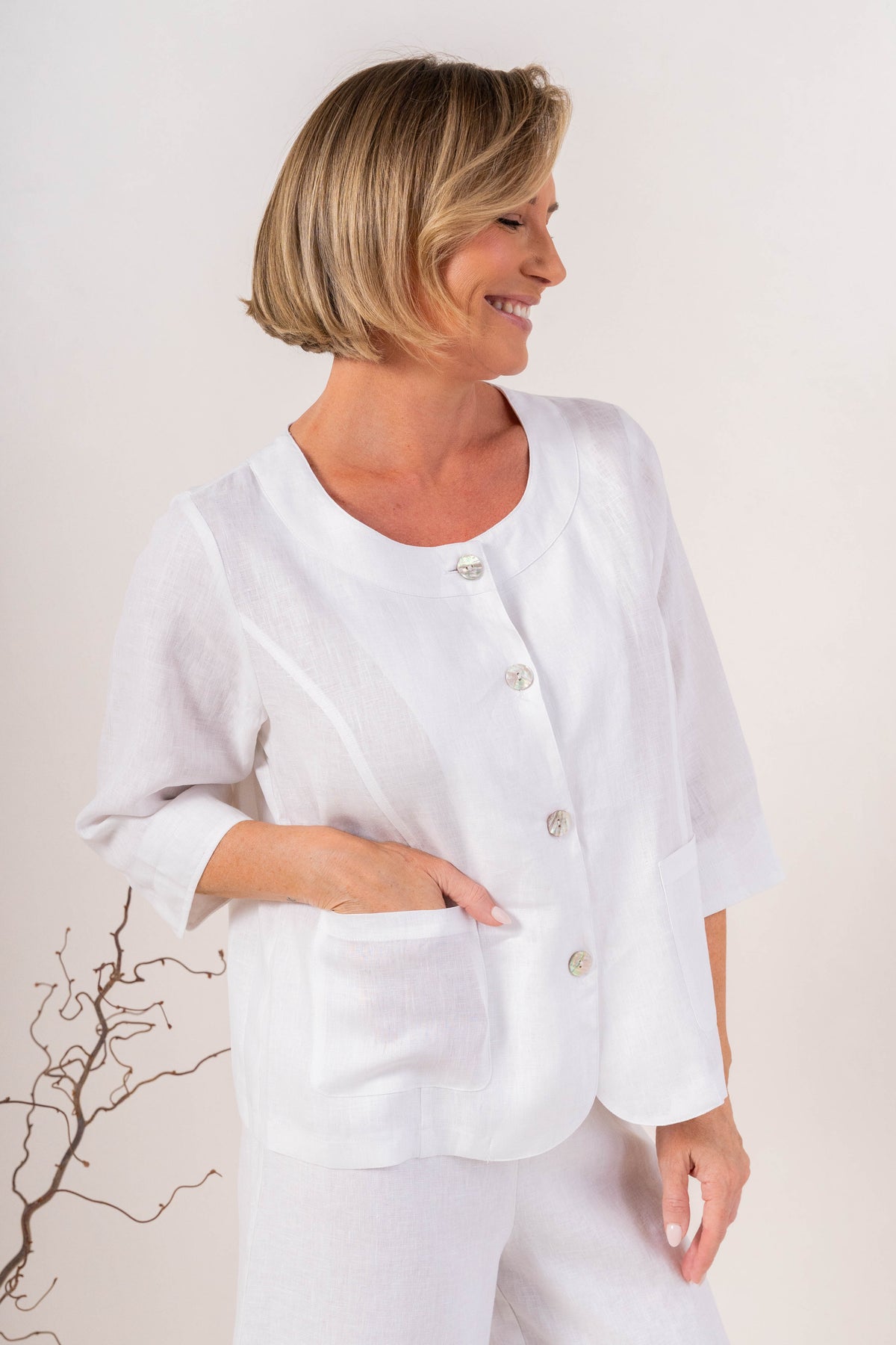 Woman modelling white linen see saw utility jacket top and against a plain background.