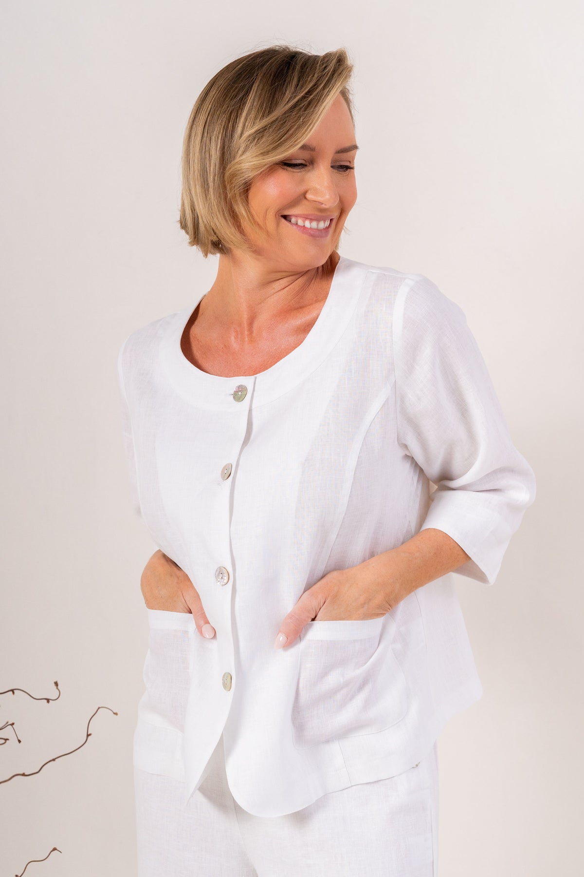 Woman modelling white linen see saw utility jacket top and matching pants and against a plain background.