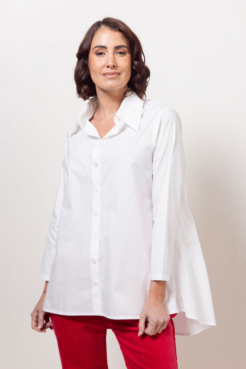 Woman wearing a white See Saw shirt in cotton with a gathered back and red cord joggers against a plain background