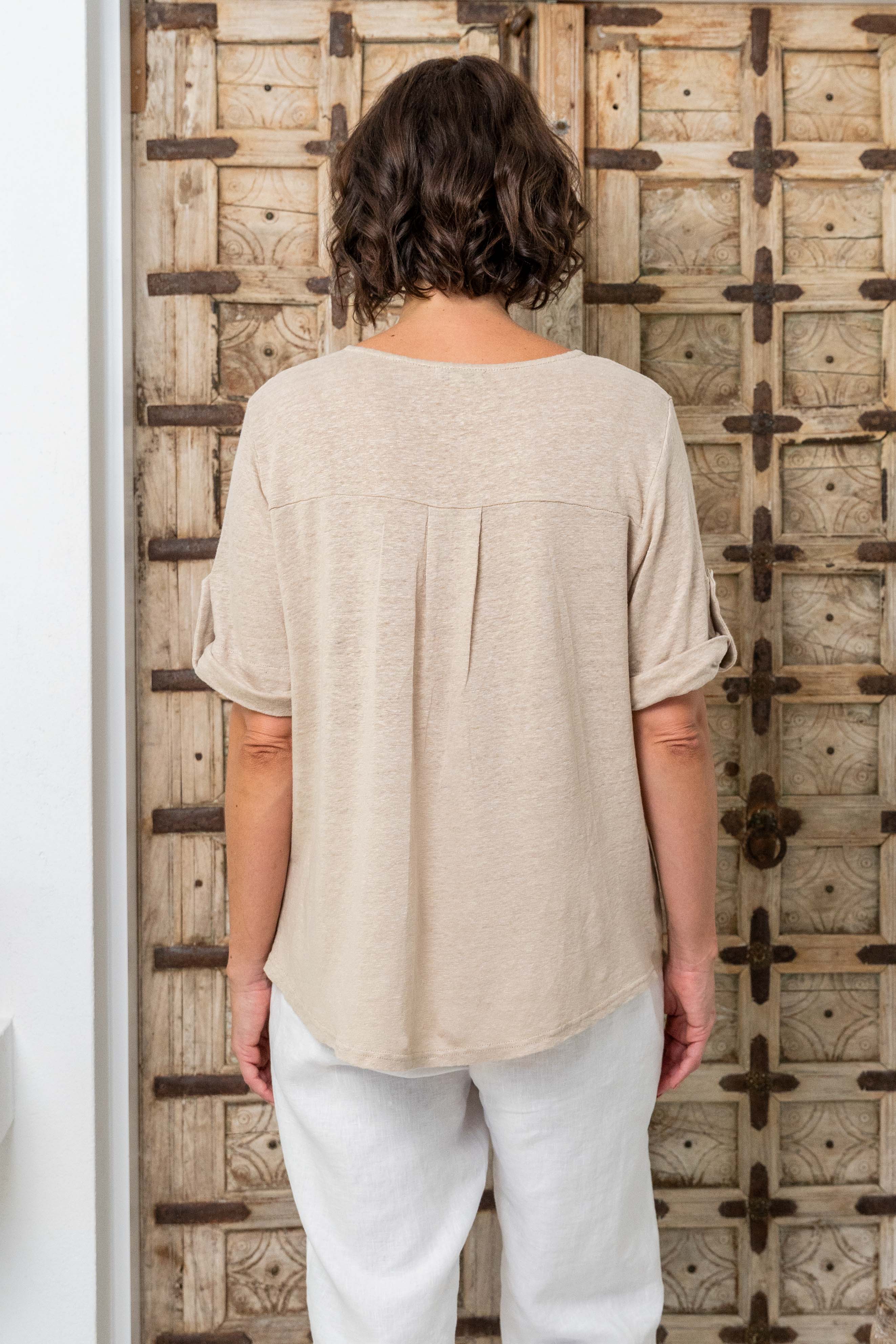Woman wearing a beige top and white pants standing against a wooden wall. See Saw Mixed Linen Blend T-shirt