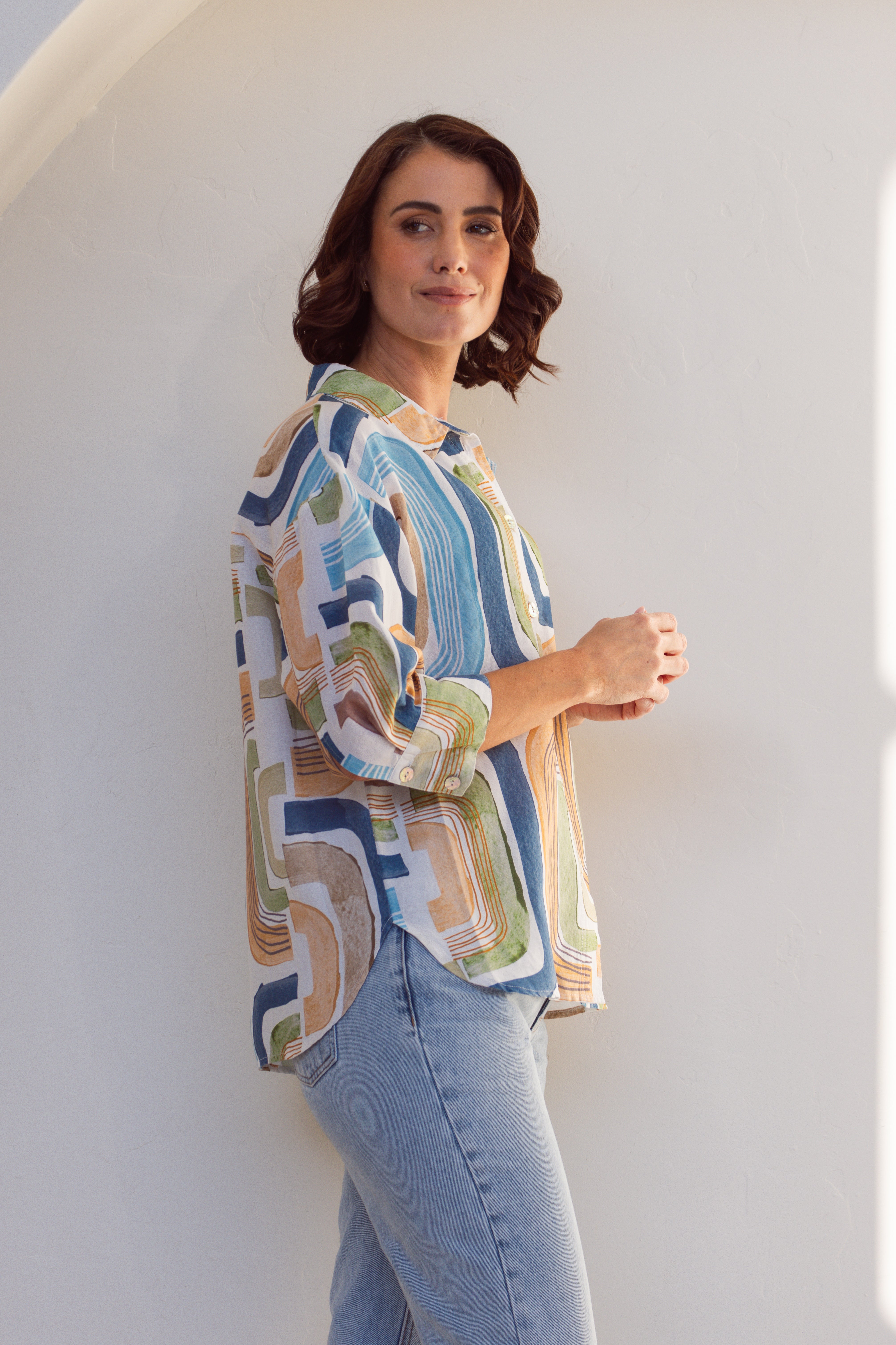 Woman wearing a patterned linen See Saw shirt and jeans against a white background