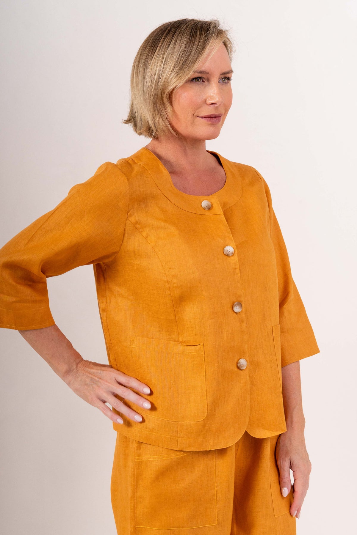 Woman modelling marigold linen see saw utility jacket top and marigold pants and against a plain background.