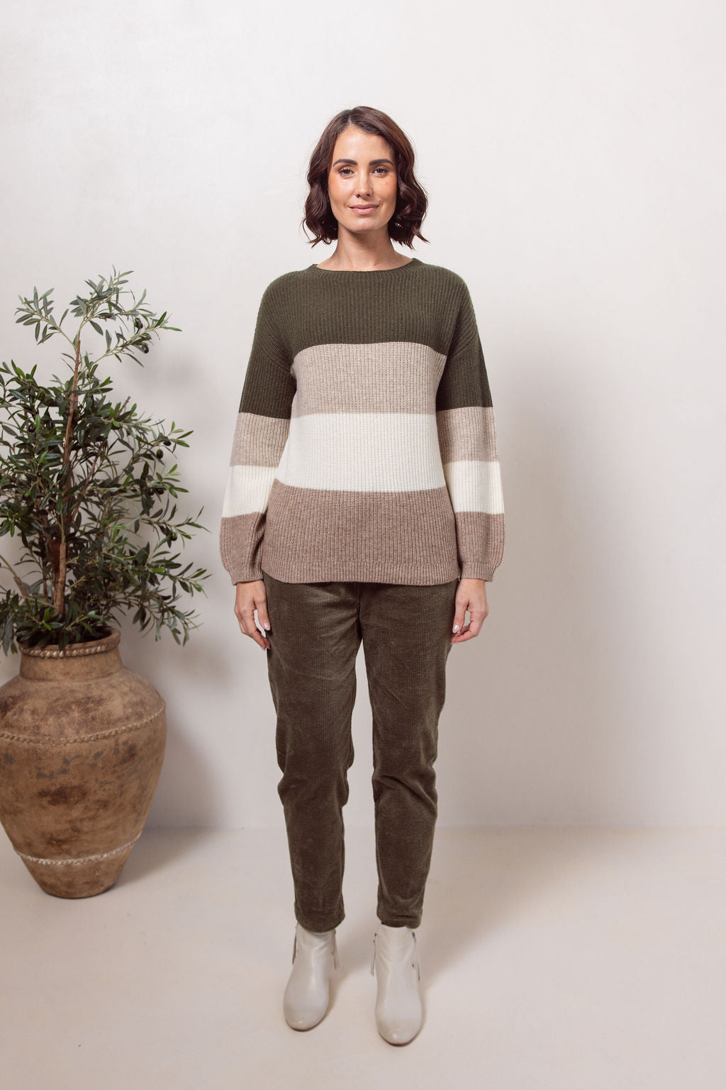 Woman wearing a khaki, beige and white striped See Saw sweater against a plain background