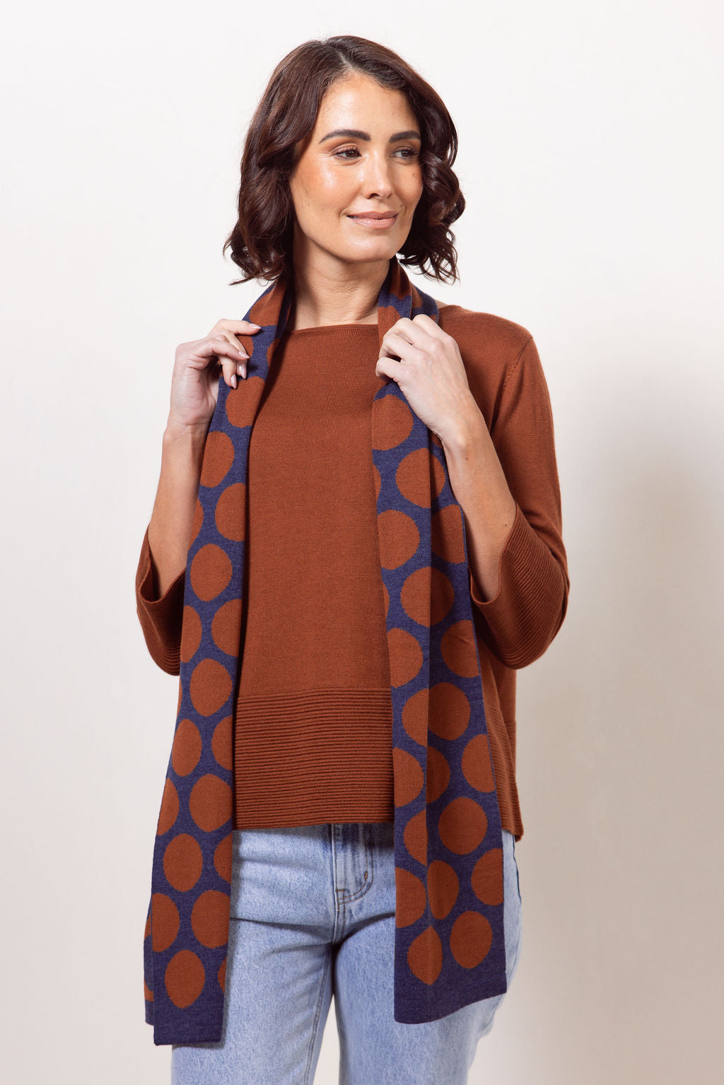 Woman wearing a copper See Saw Merino Wool sweater and patterned scarf against a white background