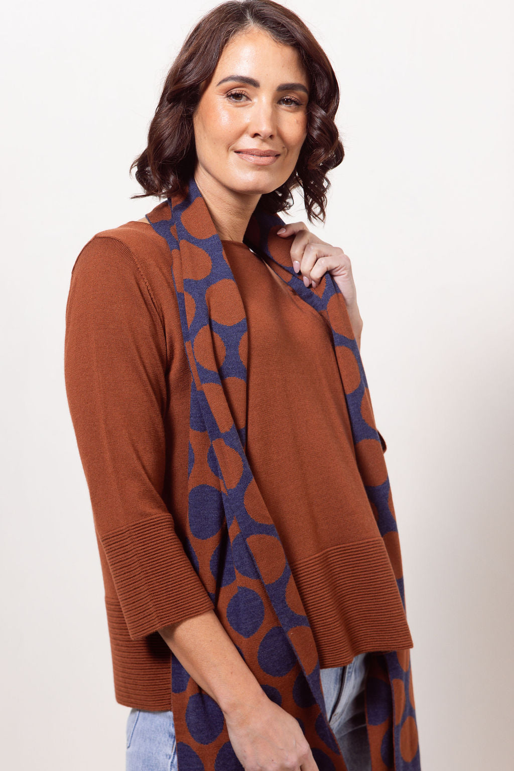 Woman wearing a copper See Saw Merino Wool sweater and patterned scarf against a white background