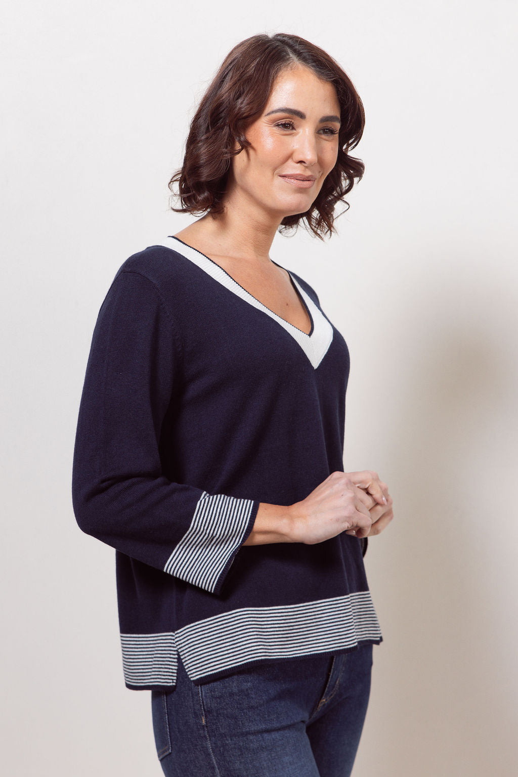 Woman wearing a navy sweater with white trim on a plain background