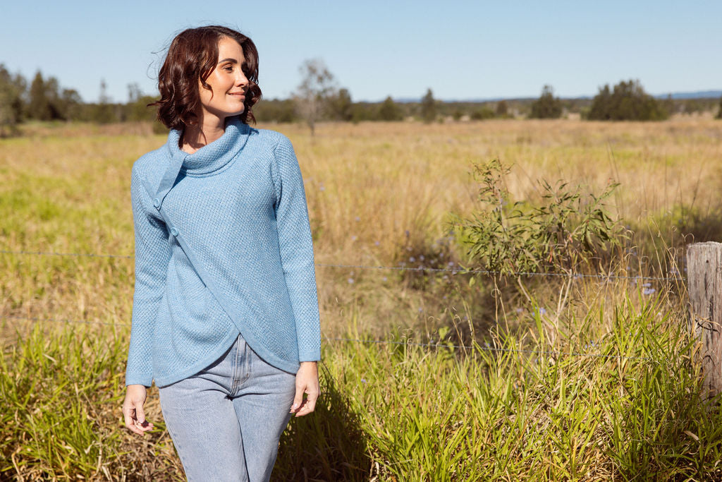 Woman wearing a powder blue Cowl Neck Moss Stitch See Saw sweater with an outdoor background
