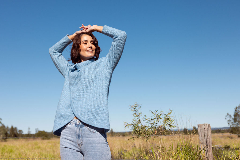 Woman wearing a powder blue Cowl Neck Moss Stitch See Saw sweater with an outdoor background