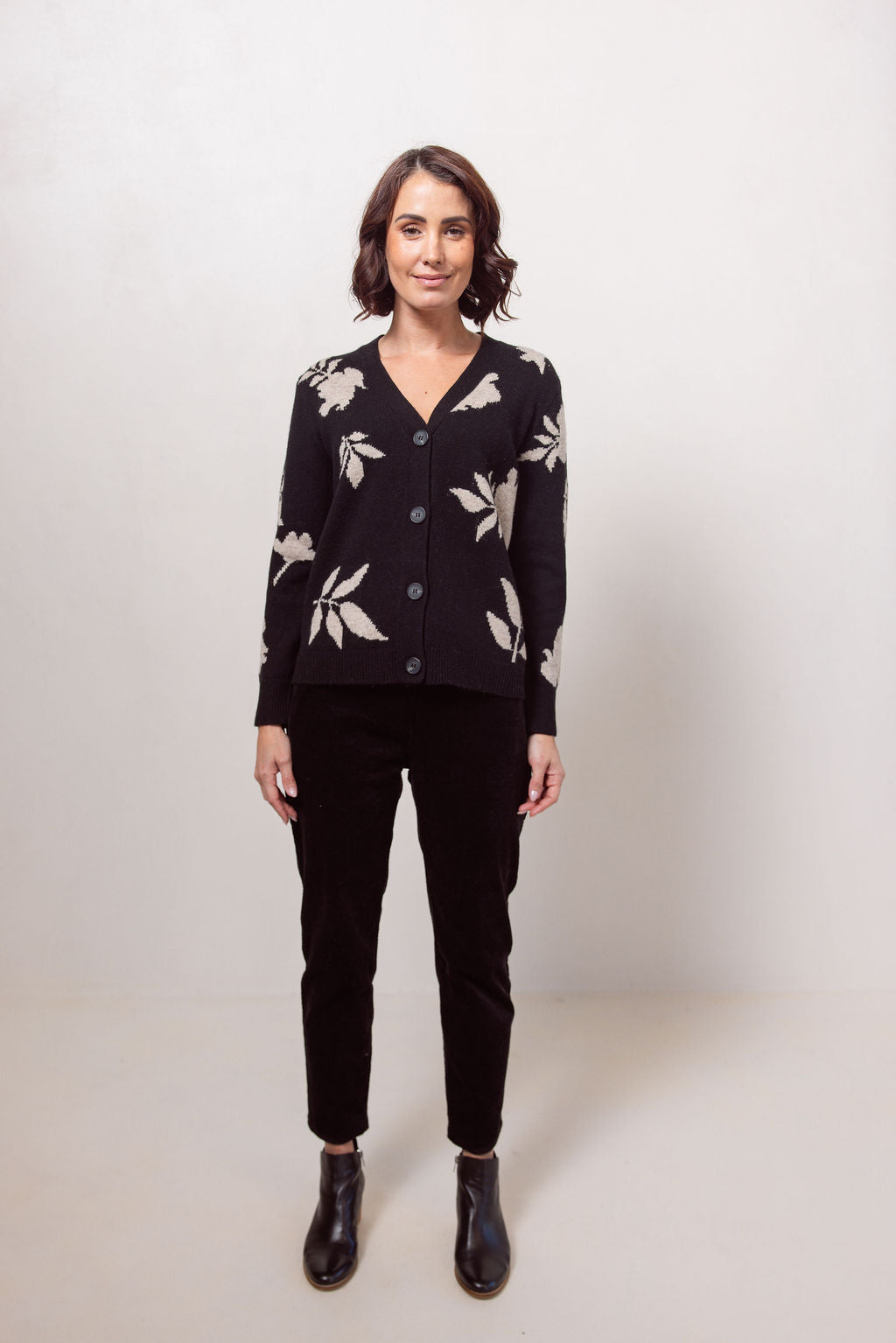 Woman wearing a black See Saw cardigan with white floral patterns against a plain background