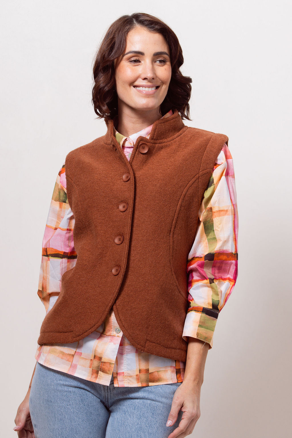Woman wearing a copper See Saw vest over a plaid shirt with a plain background