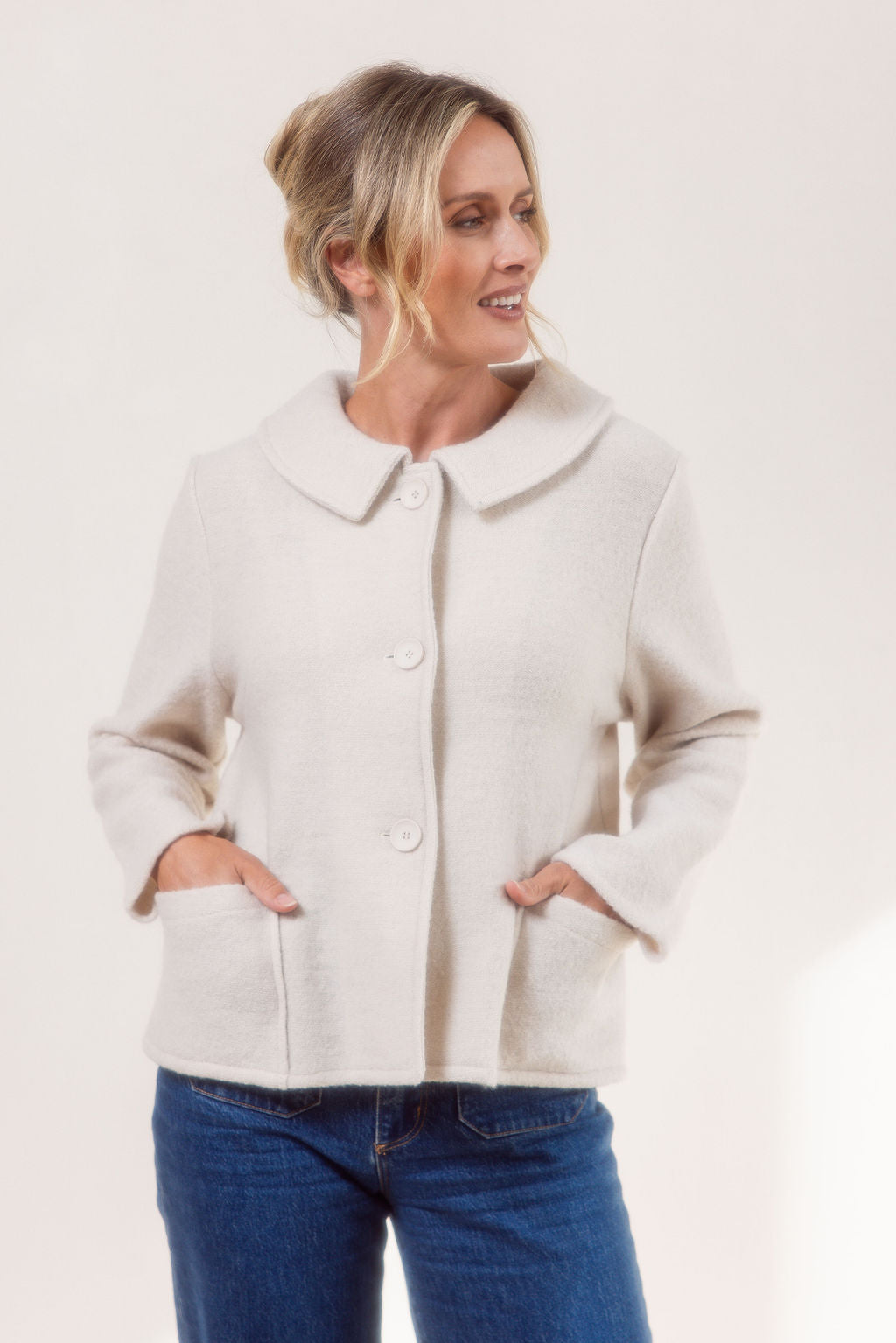 Woman wearing a cream See Saw boiled wool jacket and blue jeans on a white background