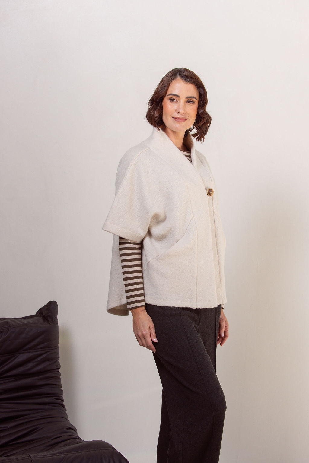 Woman wearing a See Saw boiled wool cream-colored cape jacket with striped sleeves against a plain background