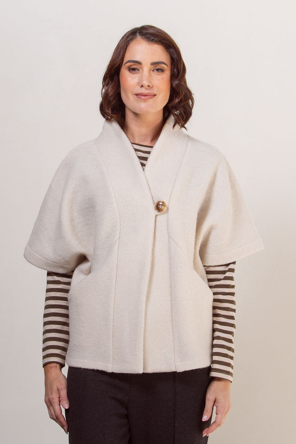 Woman wearing a See Saw boiled wool cream-colored cape jacket with striped sleeves against a plain background