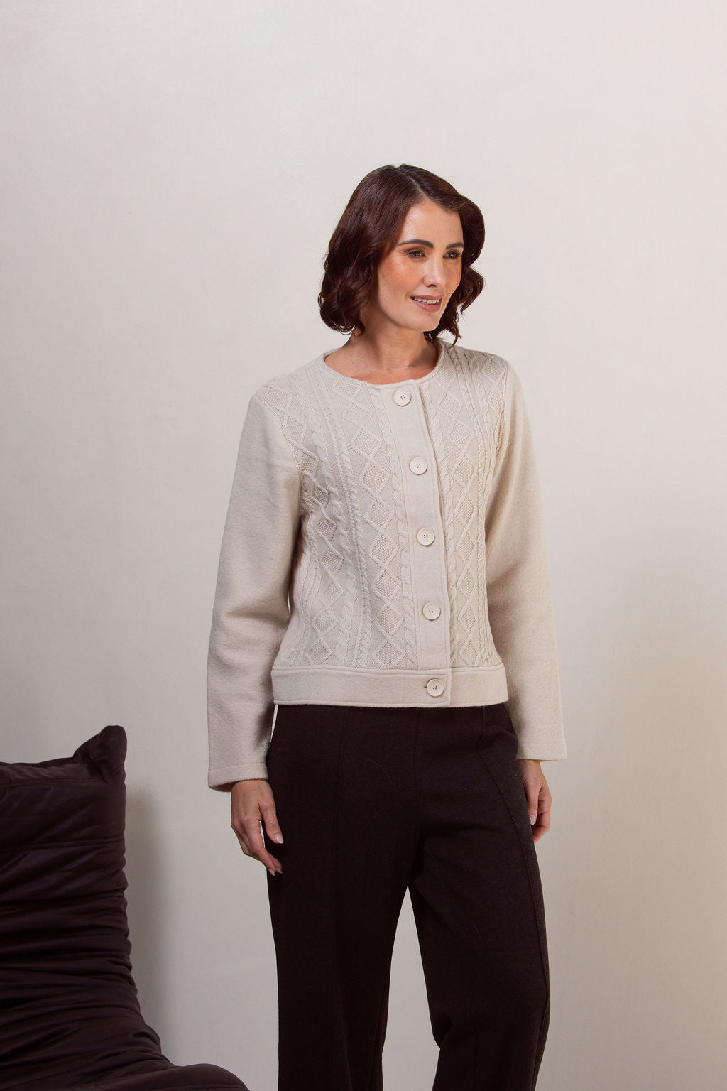 Woman wearing a boiled wool See Saw cream-colored cable knit cardigan against a plain background