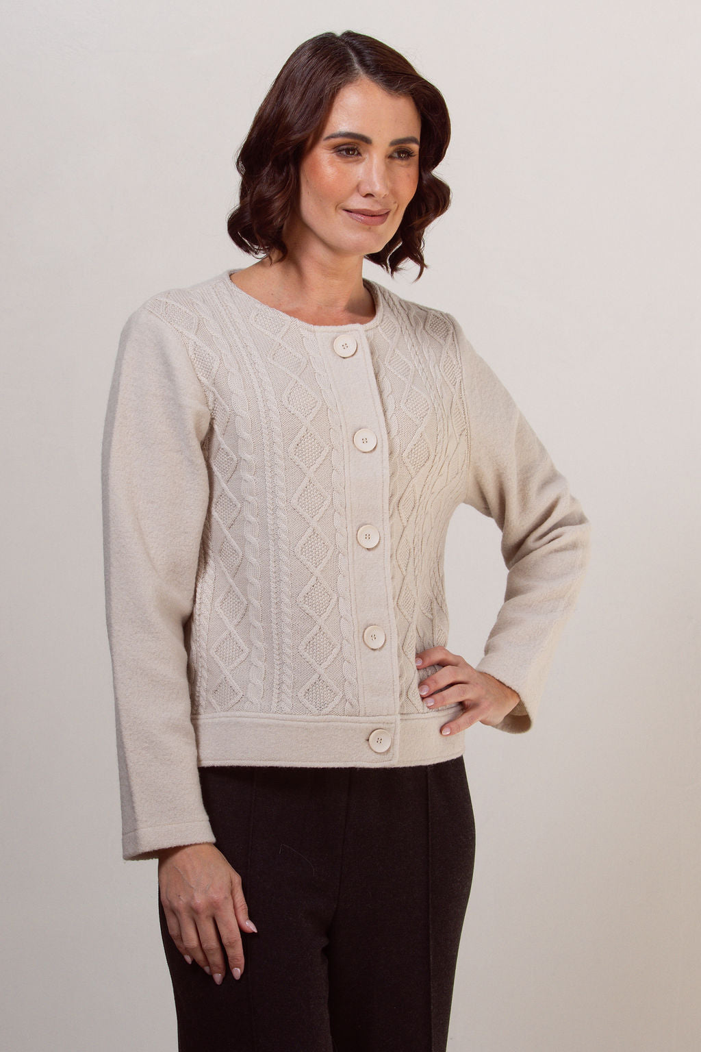Woman wearing a boiled wool See Saw cream-colored cable knit cardigan against a plain background
