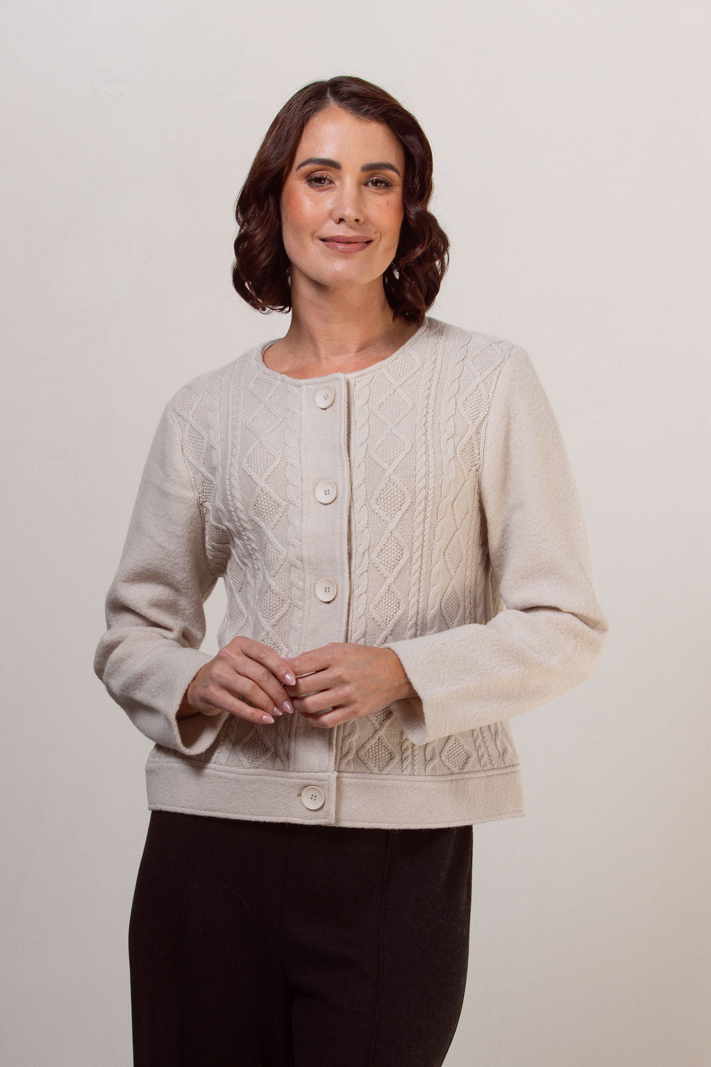 Woman wearing a boiled wool See Saw cream-colored cable knit cardigan against a plain background