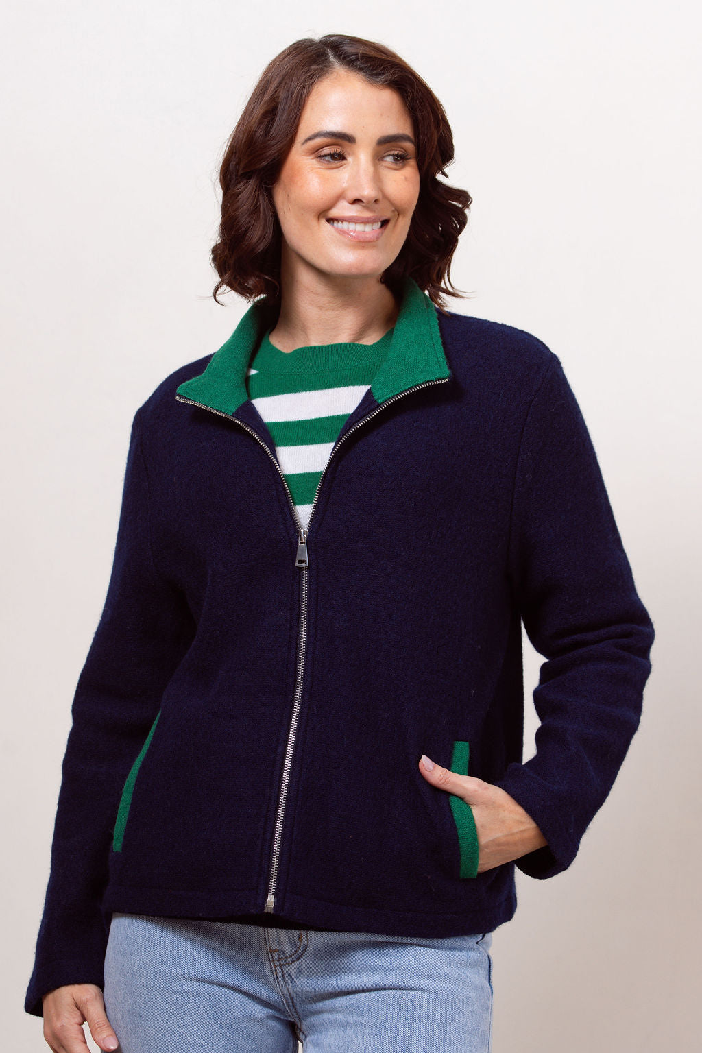 Woman wearing a navy jacket with green accents on a plain background
