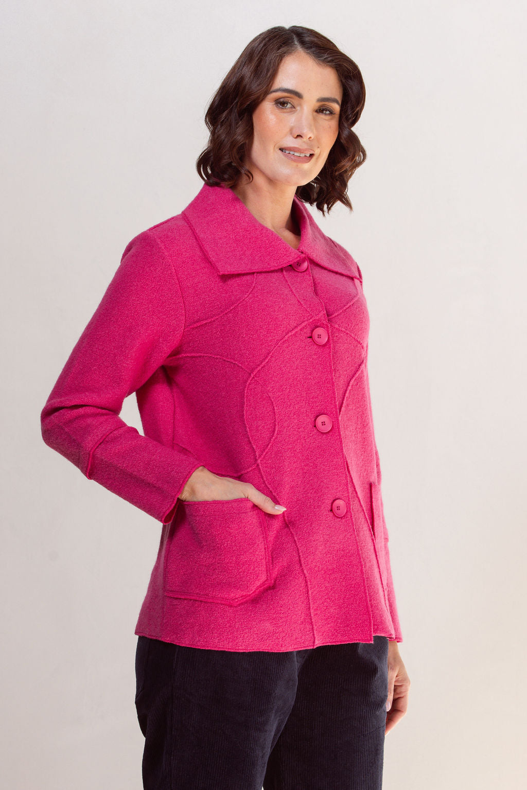 Woman wearing a bright pink See Saw Boiled wool coat against a plain background