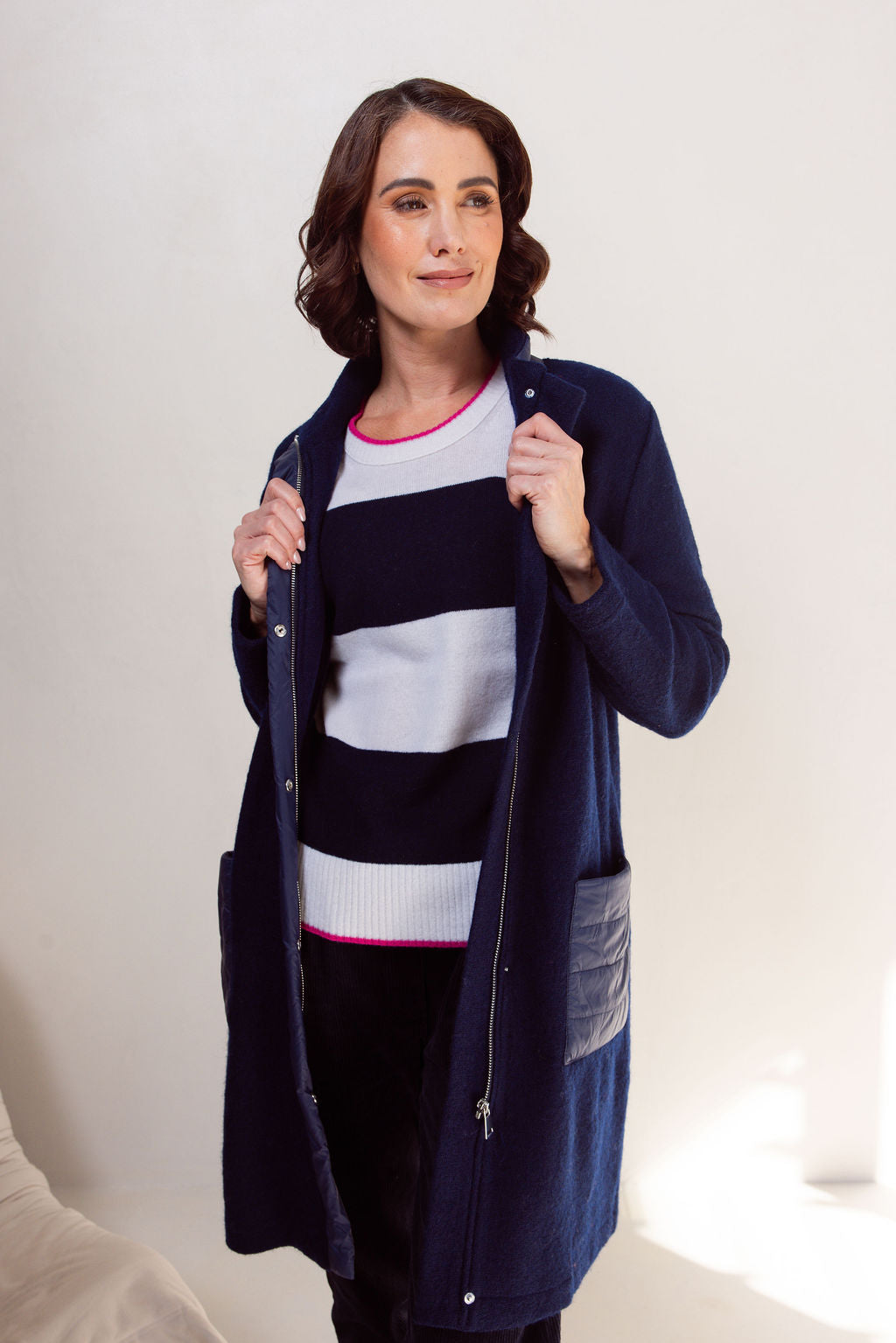Woman wearing a navy boiled wool See Saw coat over a patterned sweater on a plain background