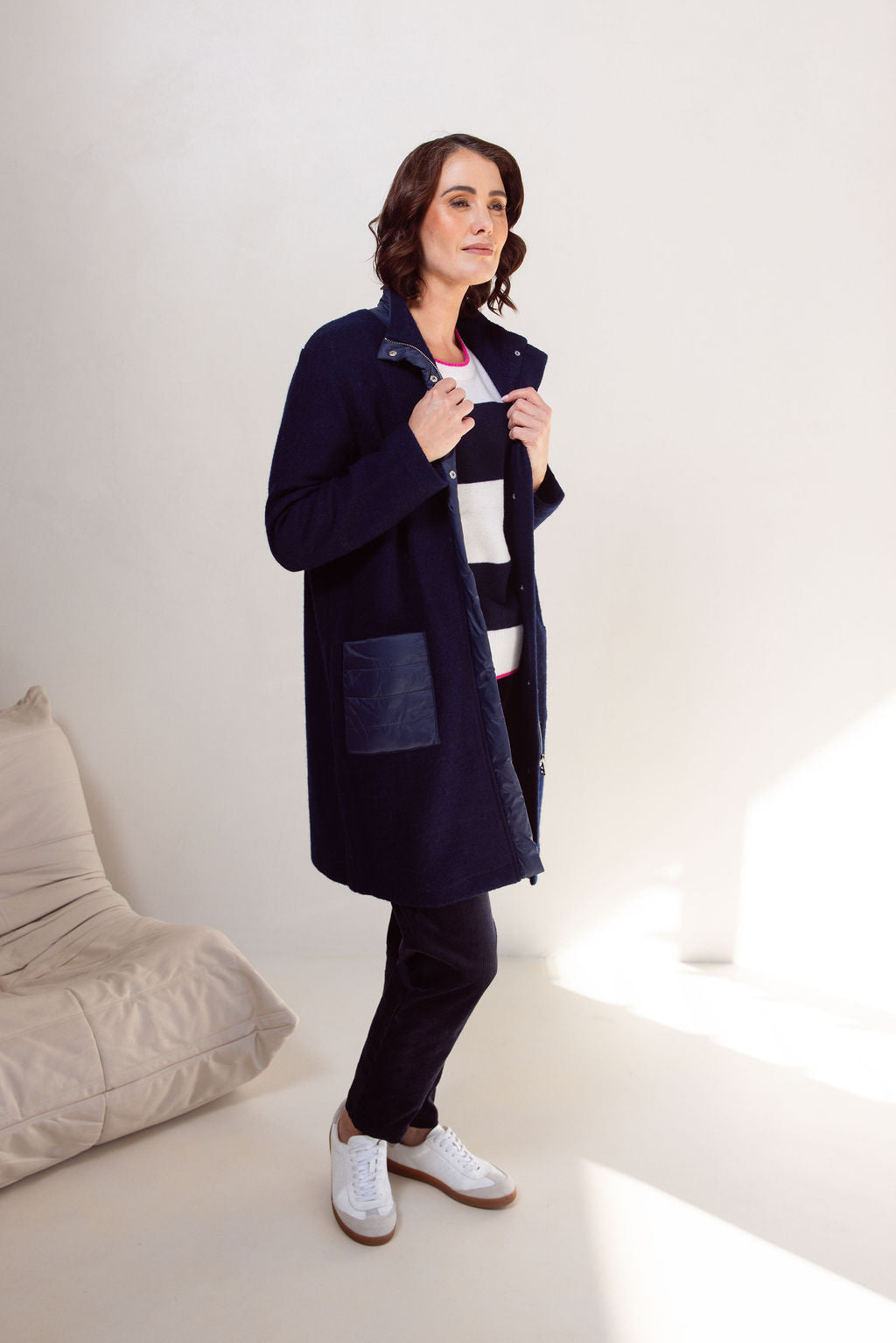 Woman wearing a navy boiled wool See Saw coat over a patterned sweater on a plain background
