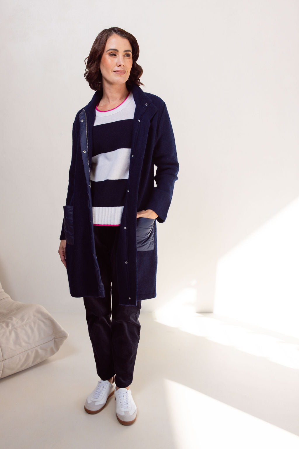 Woman wearing a navy boiled wool See Saw coat over a patterned sweater on a plain background