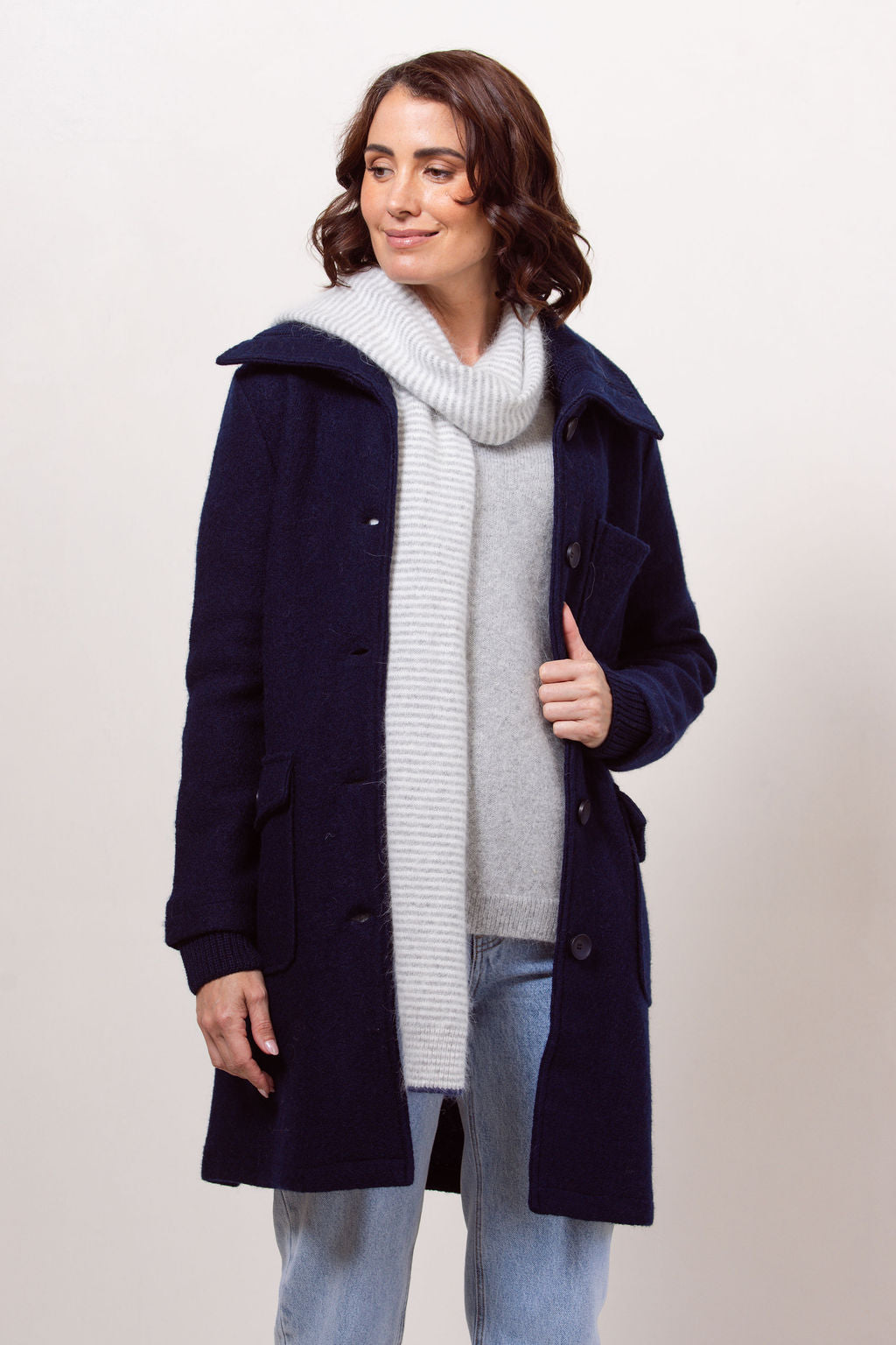 Woman wearing a navy boiled wool See Saw coat over a patterned sweater on a plain background