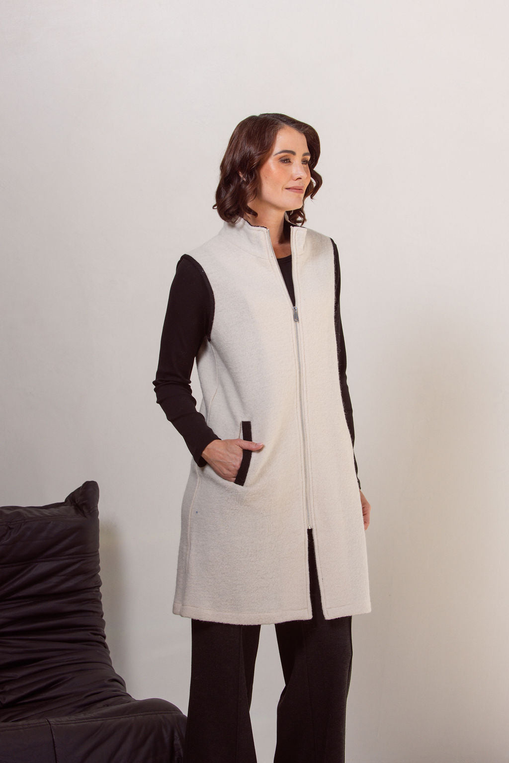 Woman wearing a cream See Saw boiled wool vest over a black long-sleeve shirt against a plain background