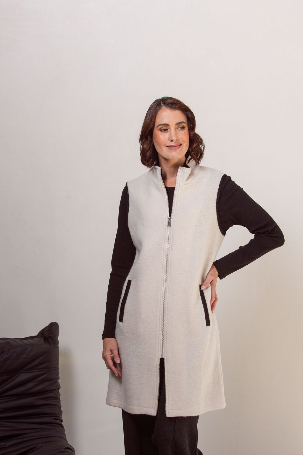 Woman wearing a cream See Saw boiled wool vest over a black long-sleeve shirt against a plain background