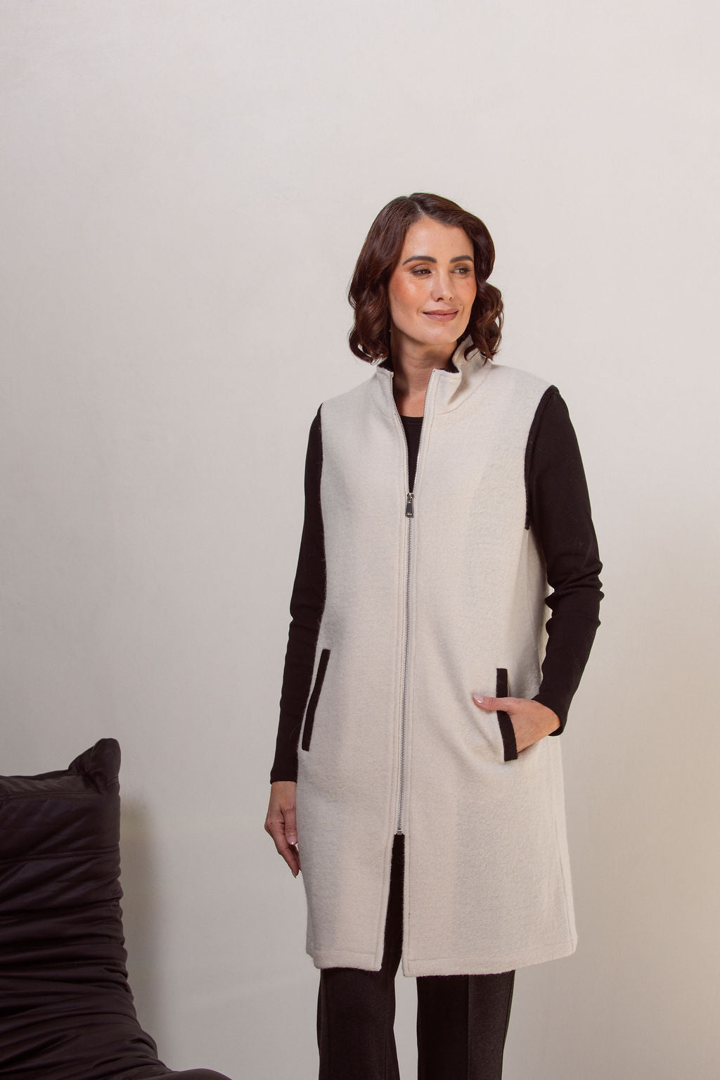 Woman wearing a cream See Saw boiled wool vest over a black long-sleeve shirt against a plain background
