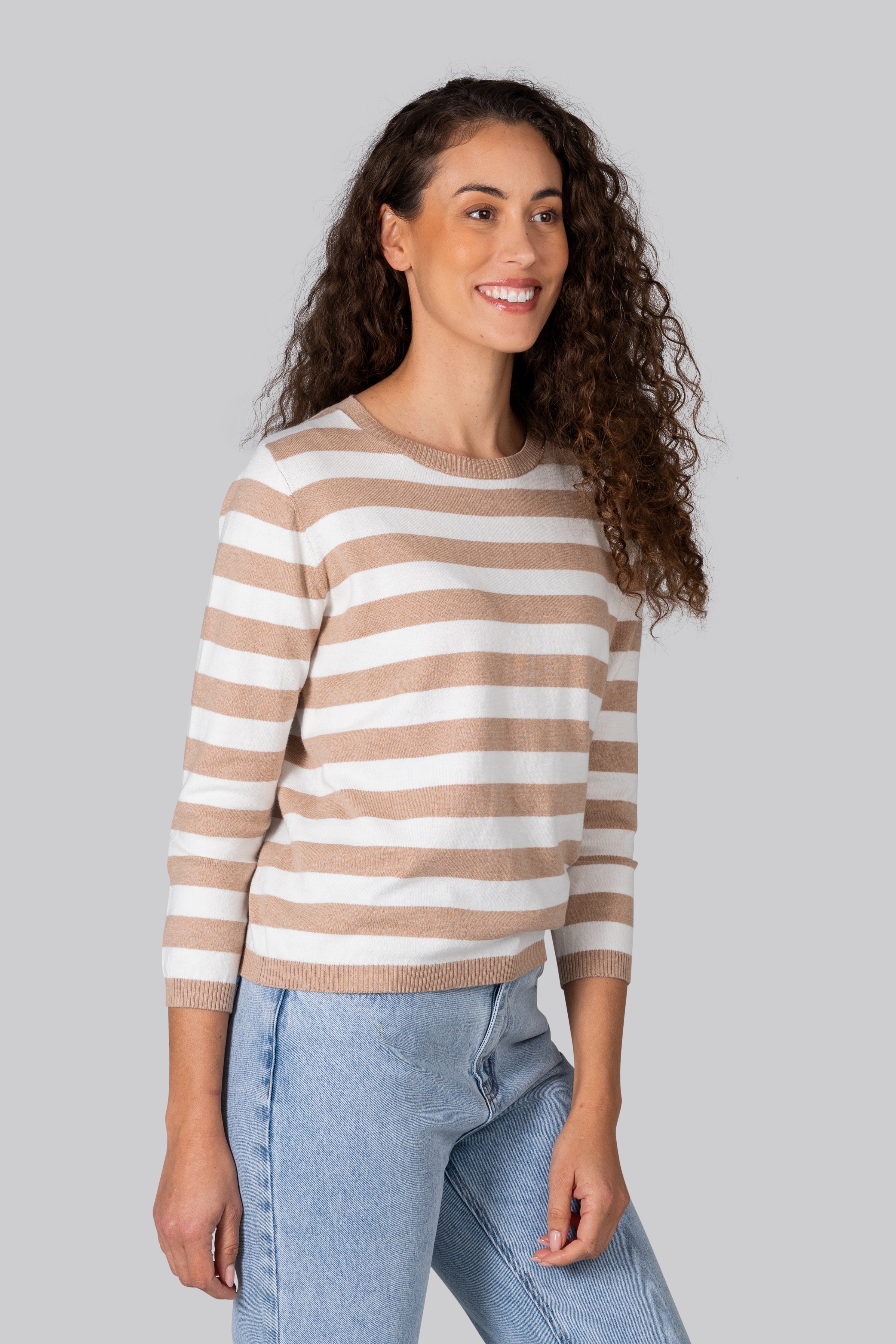 Woman wearing a cotton cashmere Kaleido striped sweater and jeans against a plain background