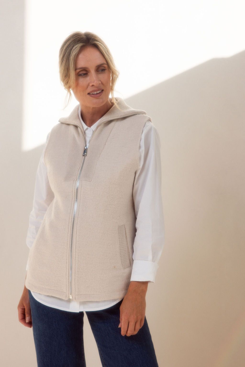 Woman wearing a See Saw cream zip-up vest over a white shirt with a plain background