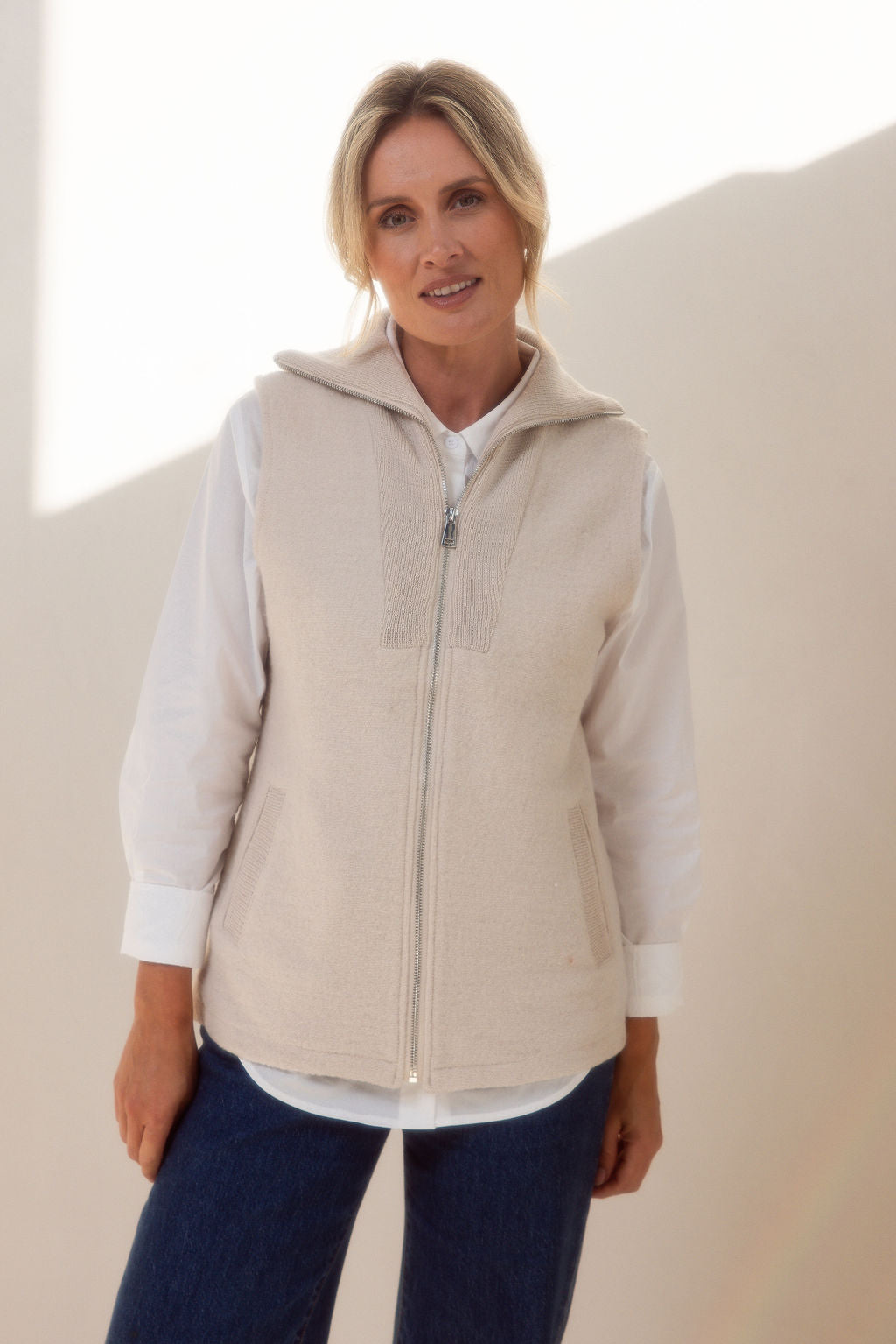 Woman wearing a See Saw cream zip-up vest over a white shirt with a plain background