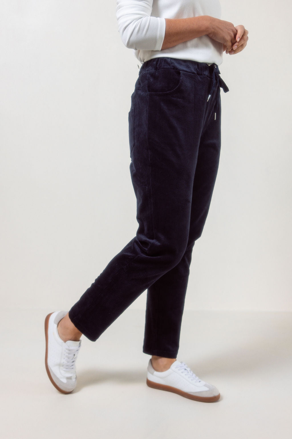 Person wearing See Saw Navy corduroy jogger pants and white sneakers on a plain background