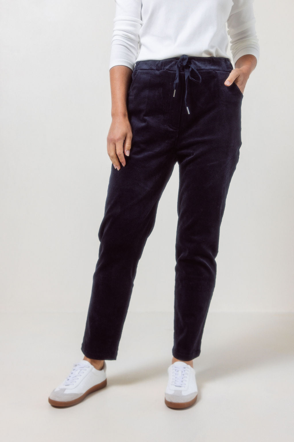 Person wearing See Saw Navy corduroy jogger pants and white sneakers on a plain background