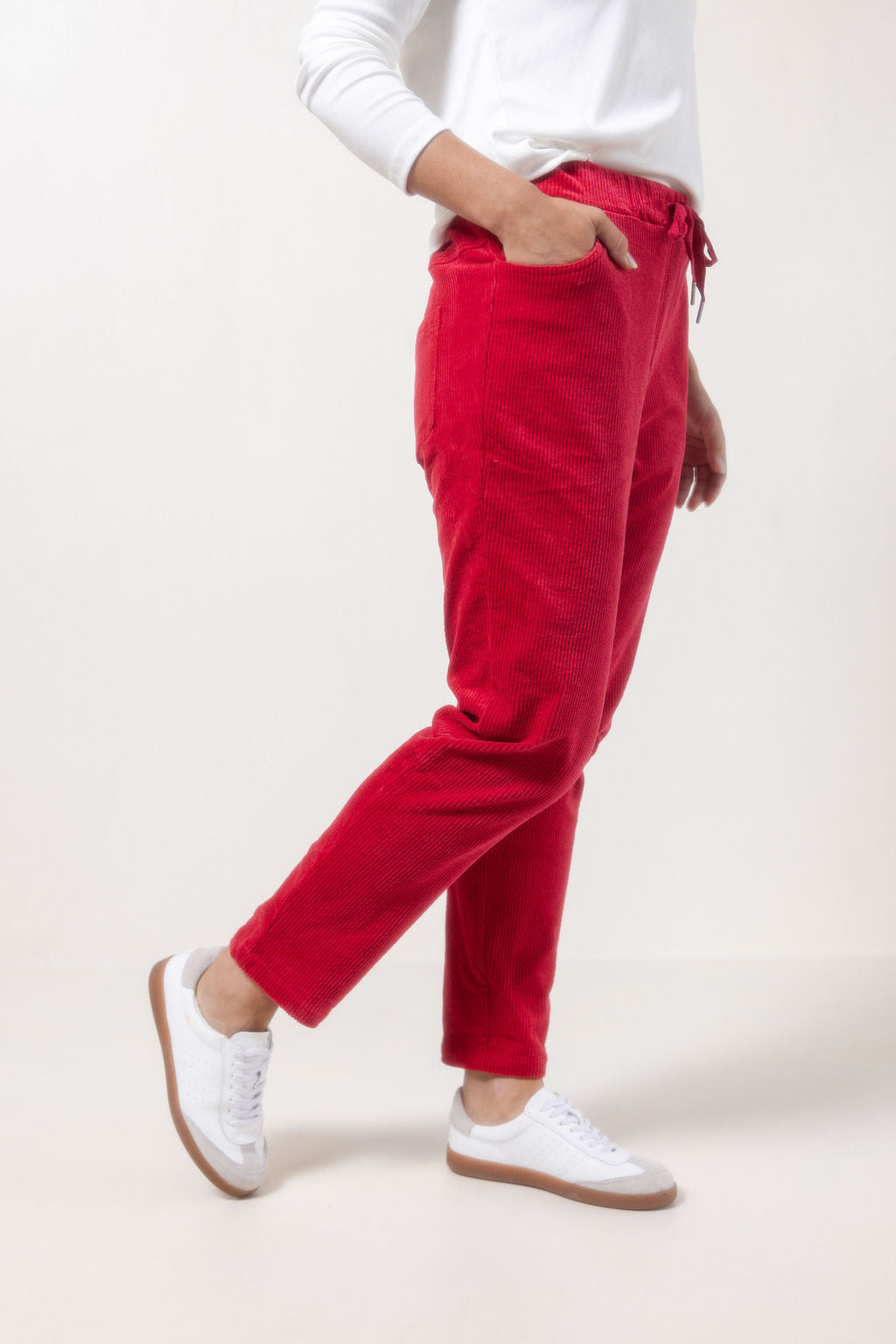 Person wearing See Saw red corduroy jogger pants and white sneakers on a plain background