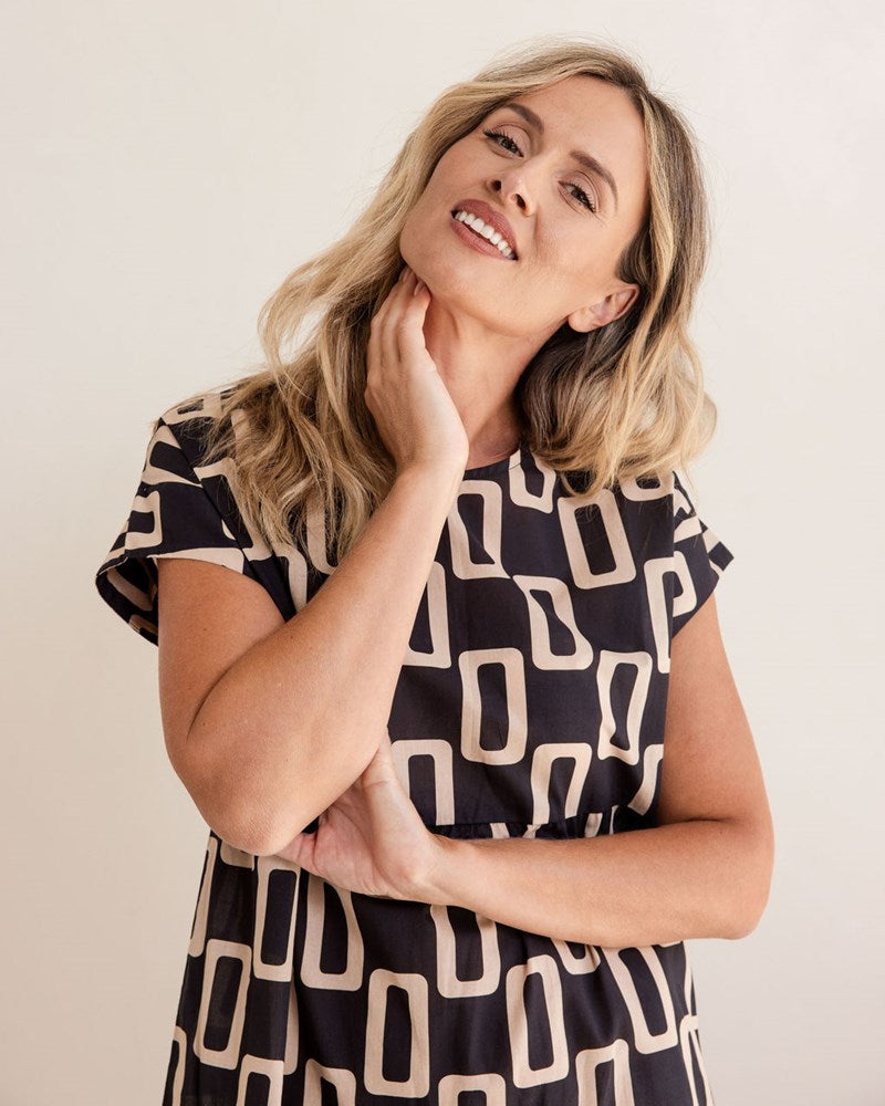 Woman wearing a black and beige patterned dress against a plain background. See Saw Cotton Tiered Dress