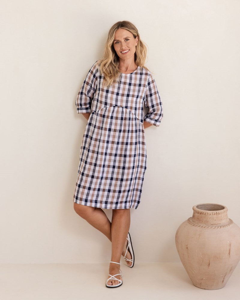 Woman wearing a blue and white checkered dress standing next to a decorative vase against a plain background. See Saw Linen Elbow Sleeve Button Back Dress