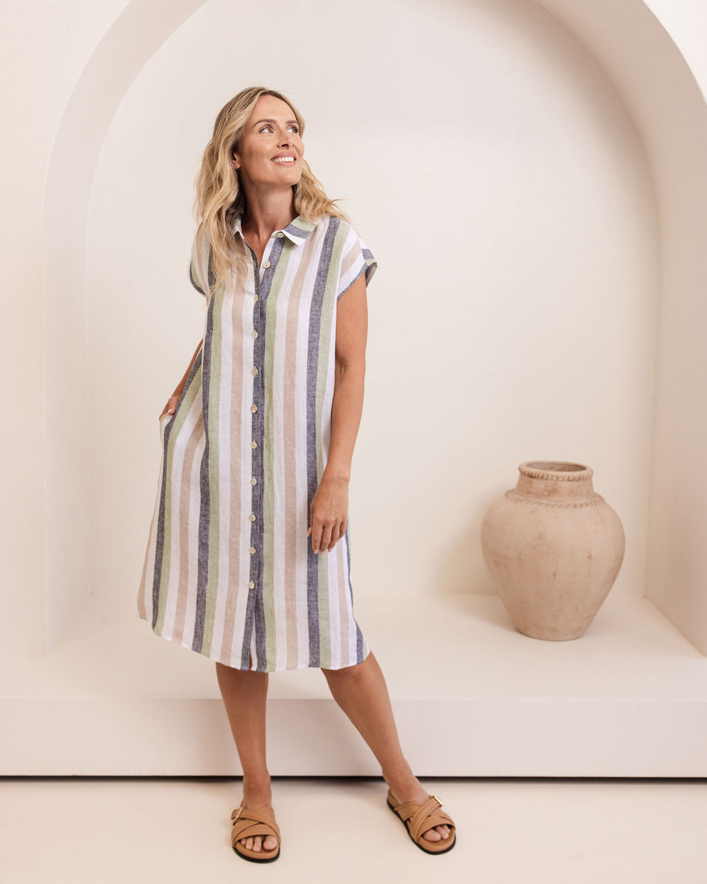 Woman wearing a striped dress standing in a minimalistic setting with a vase. See Saw Linen Stripe Extended Sleeve Dress