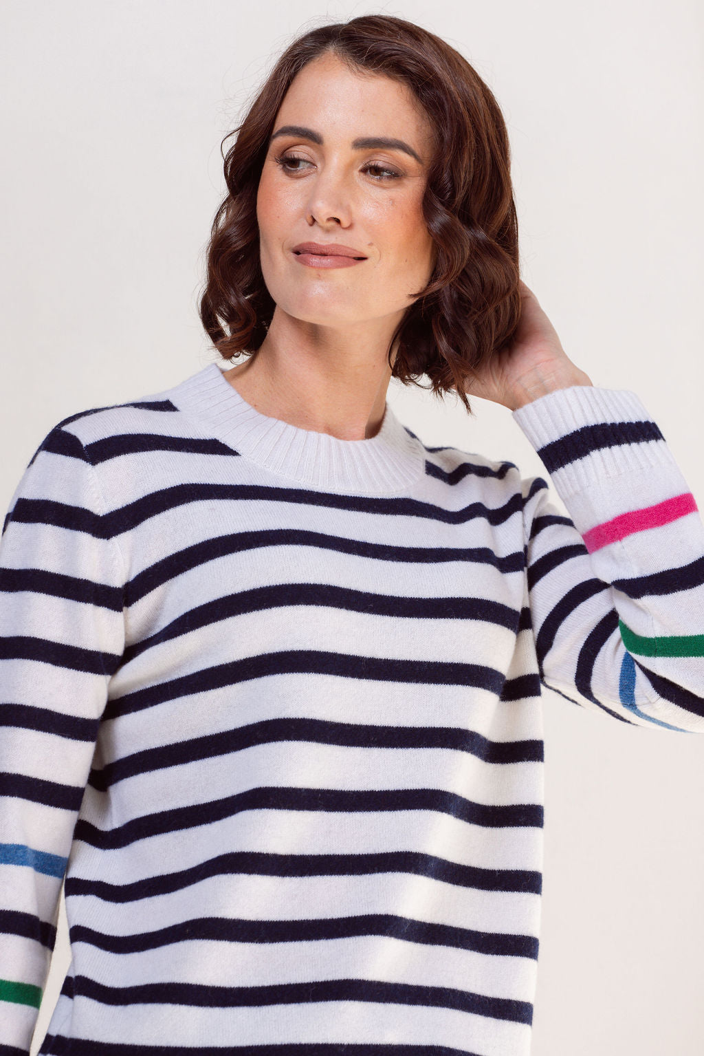 Woman wearing a striped See Saw sweater with colorful cuffs against a plain background