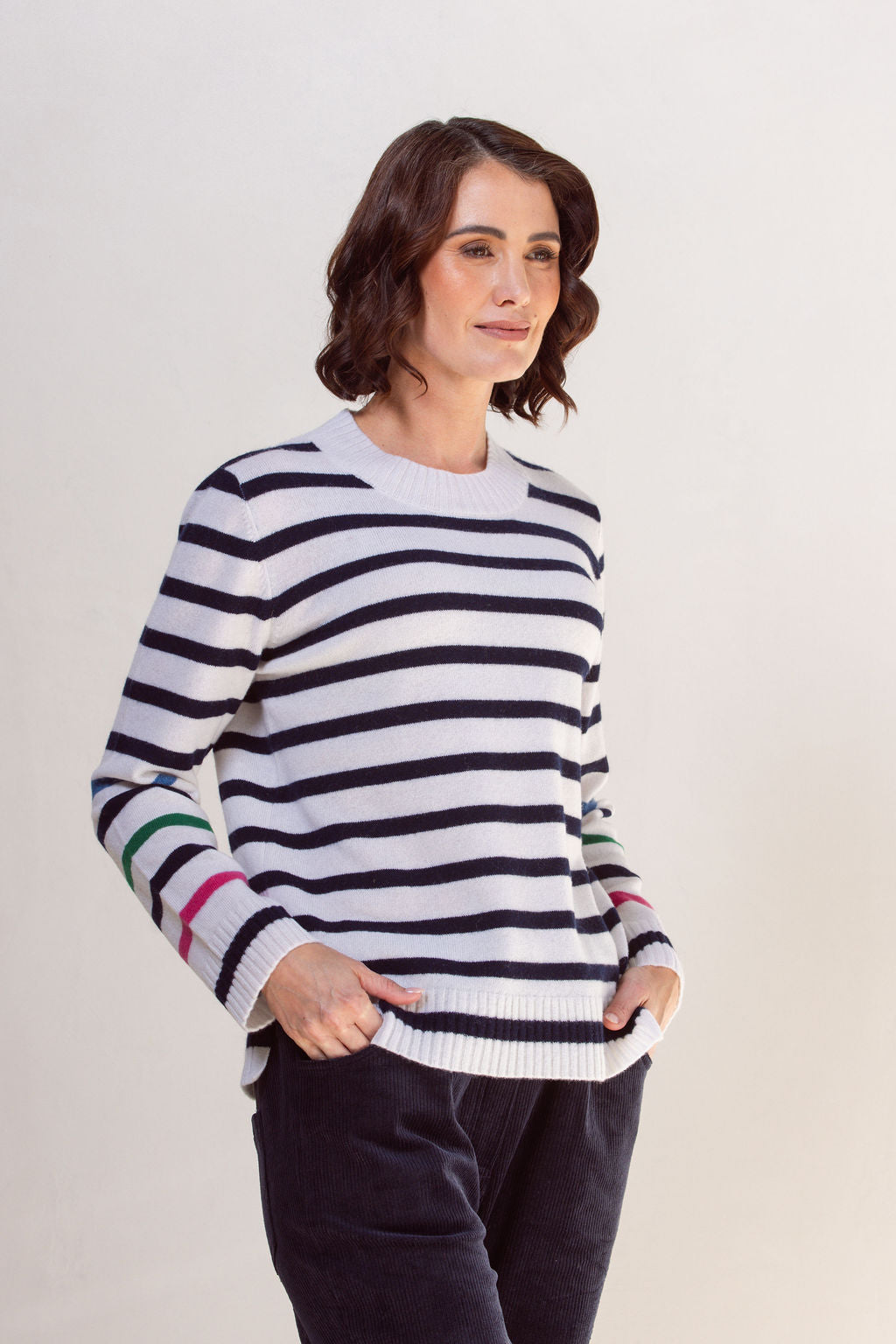 Woman wearing a striped See Saw sweater with colorful cuffs against a plain background