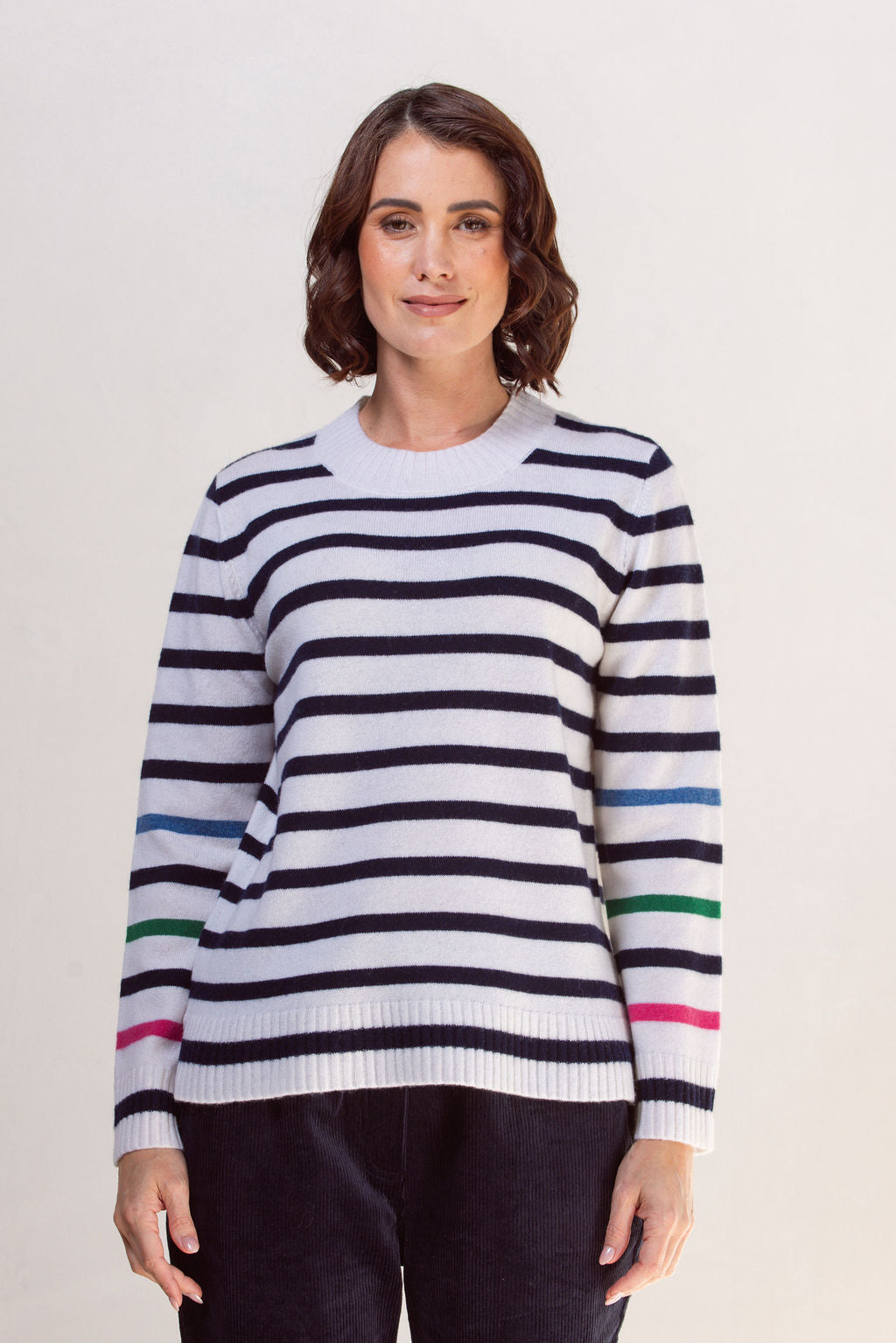Woman wearing a striped See Saw sweater with colorful cuffs against a plain background