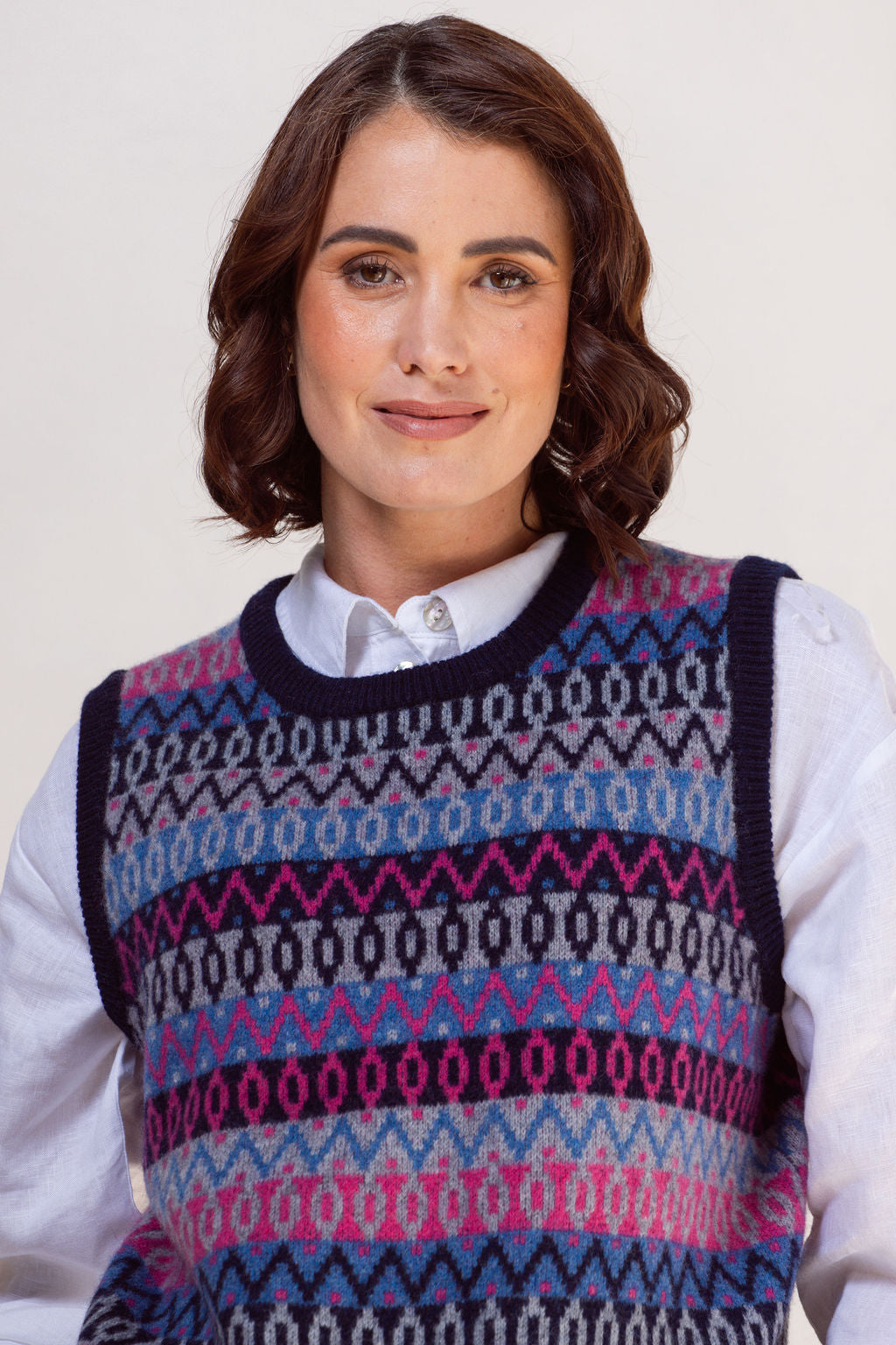 Woman wearing a See Saw jacquard patterned sweater vest over a white shirt on a plain background